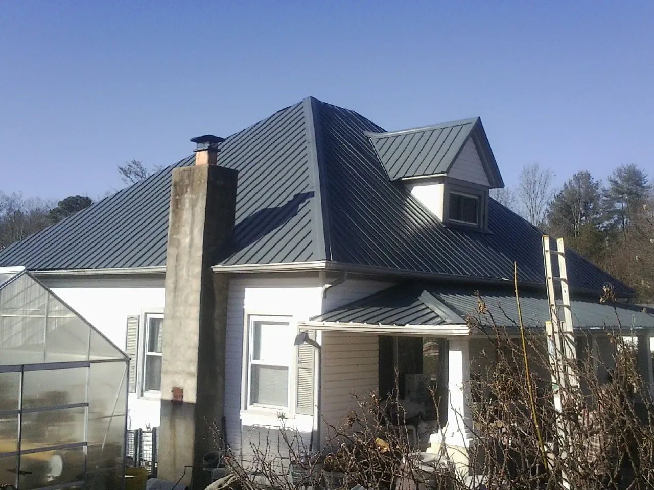 Dark blue standing seam metal roof on a white farmhouse with dormer — Slate & Tile Roof Repair by Roofing Brothers in Mooresboro