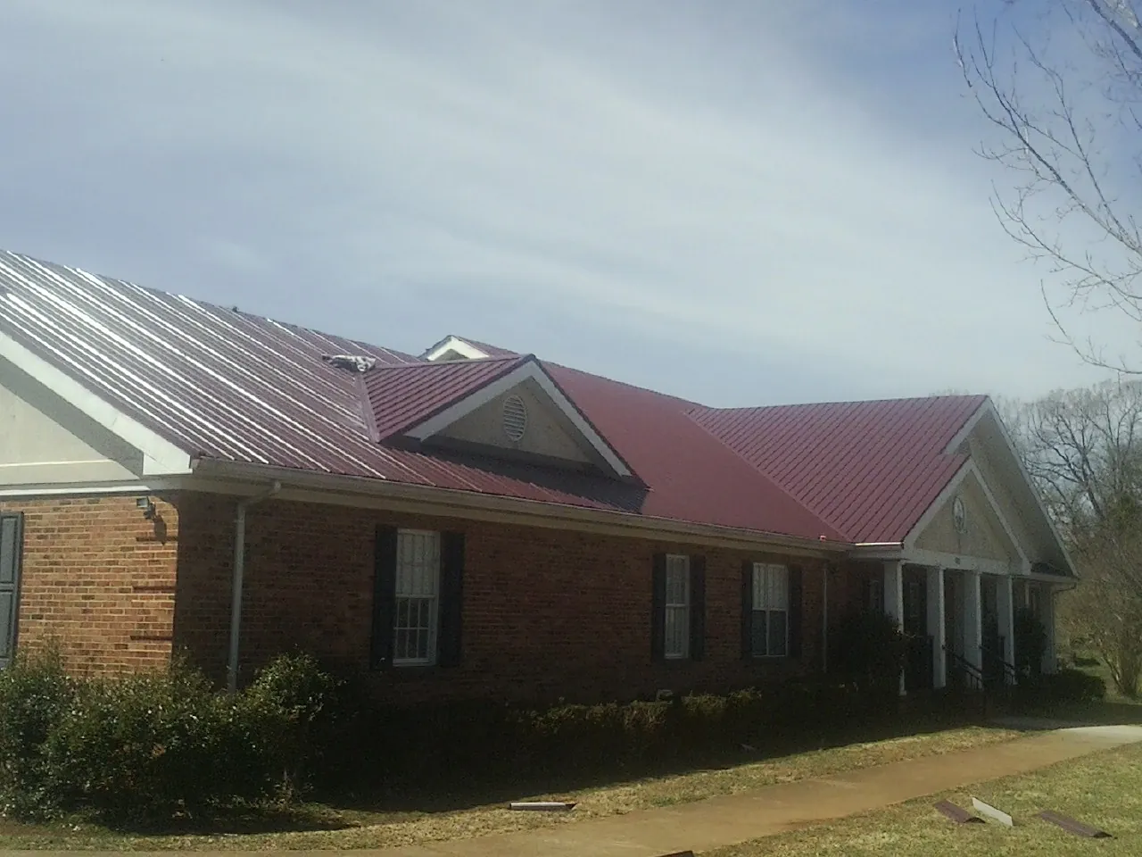 Red metal roof with gabled entries on a long brick building, from a Hail Damage Roof Repair job in Mooresboro
