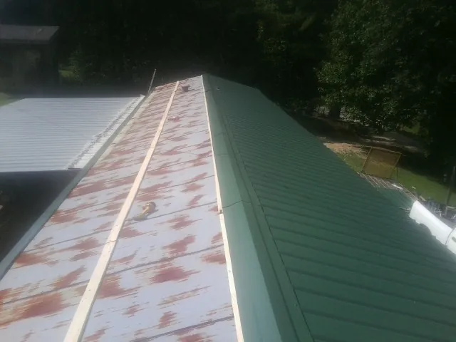Old rusted panels beside newly installed green metal roofing — Wind Damage Roof Repair by Roofing Brothers in Mooresboro