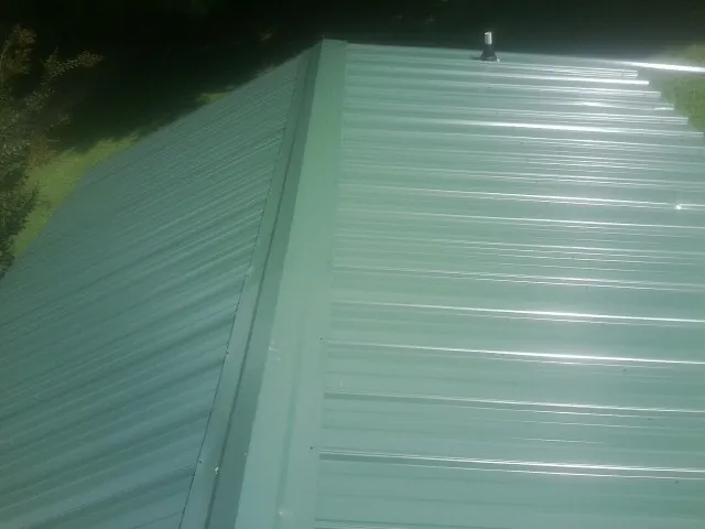New green metal panels meeting at the ridge of a roof — Flat Roof Repair work by our crew in Mooresboro