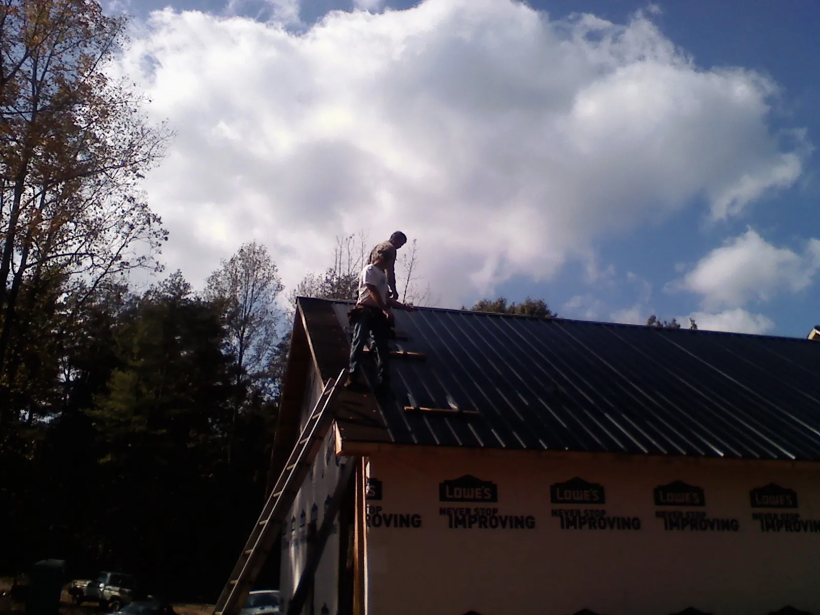 Roofer fastening dark metal panels high against a cloudy sky, from a Roof Inspection job in Mooresboro