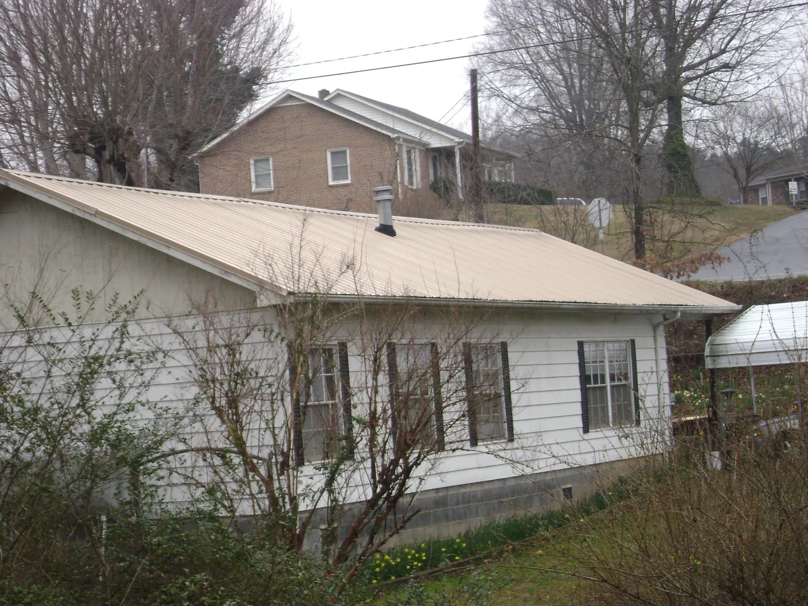 Tan metal roof on a white sided house set into a hillside — Commercial Roofing by Roofing Brothers in Mooresboro
